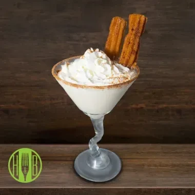 White drink with whipped cream and two churros in a martini glass.