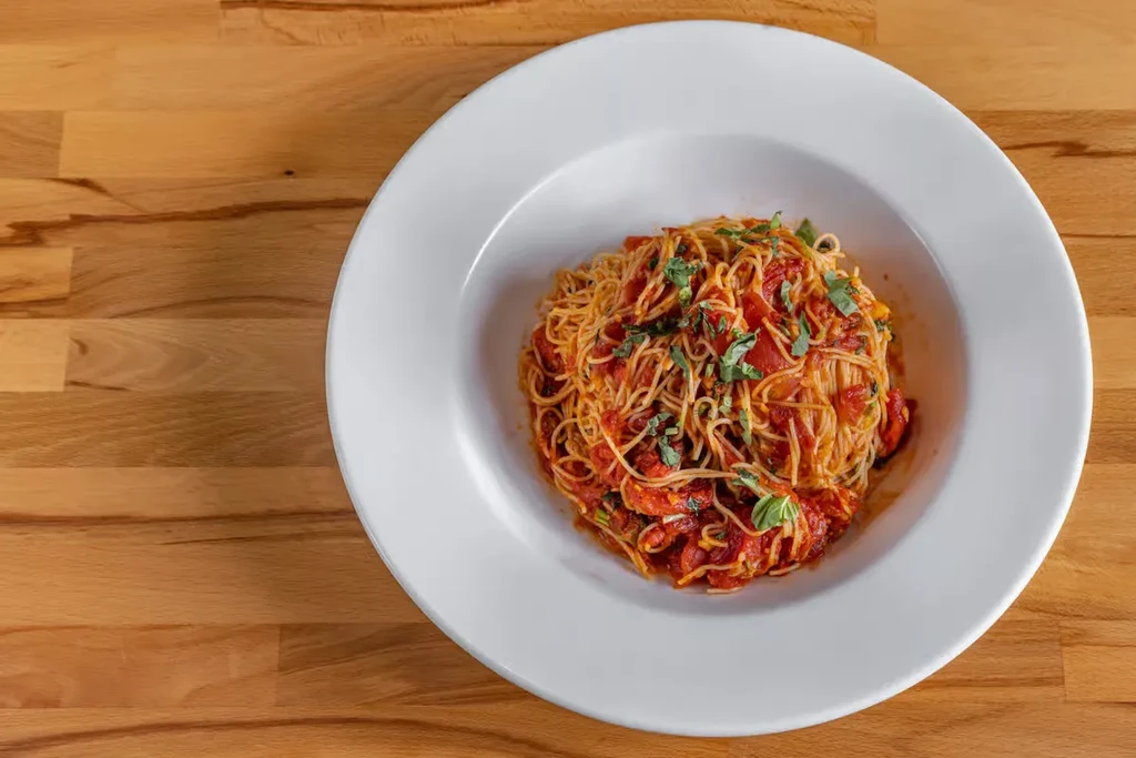 Pasta with tomato sauce and basil in a white bowl.
