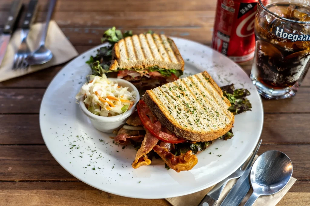 A club sandwich, coleslaw, and soda on a wooden table.