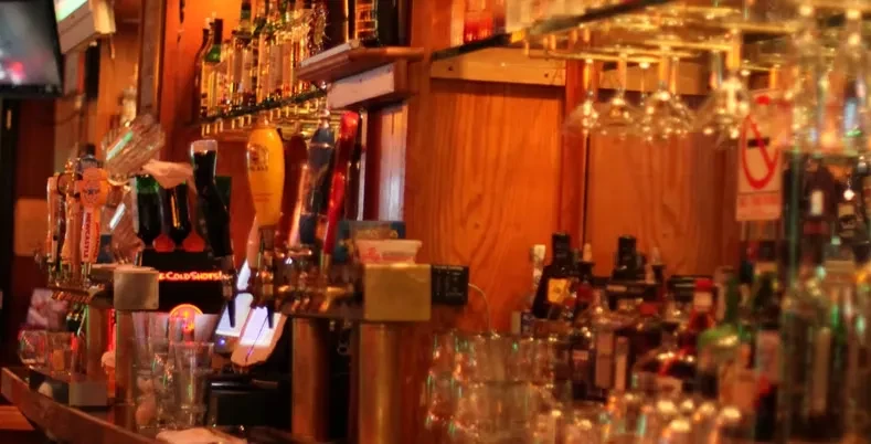 A blurry, warm-lit image of a bar with beer taps and liquor bottles.