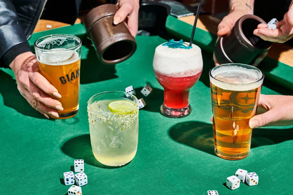 Hands holding drinks and dice on a green tabletop.