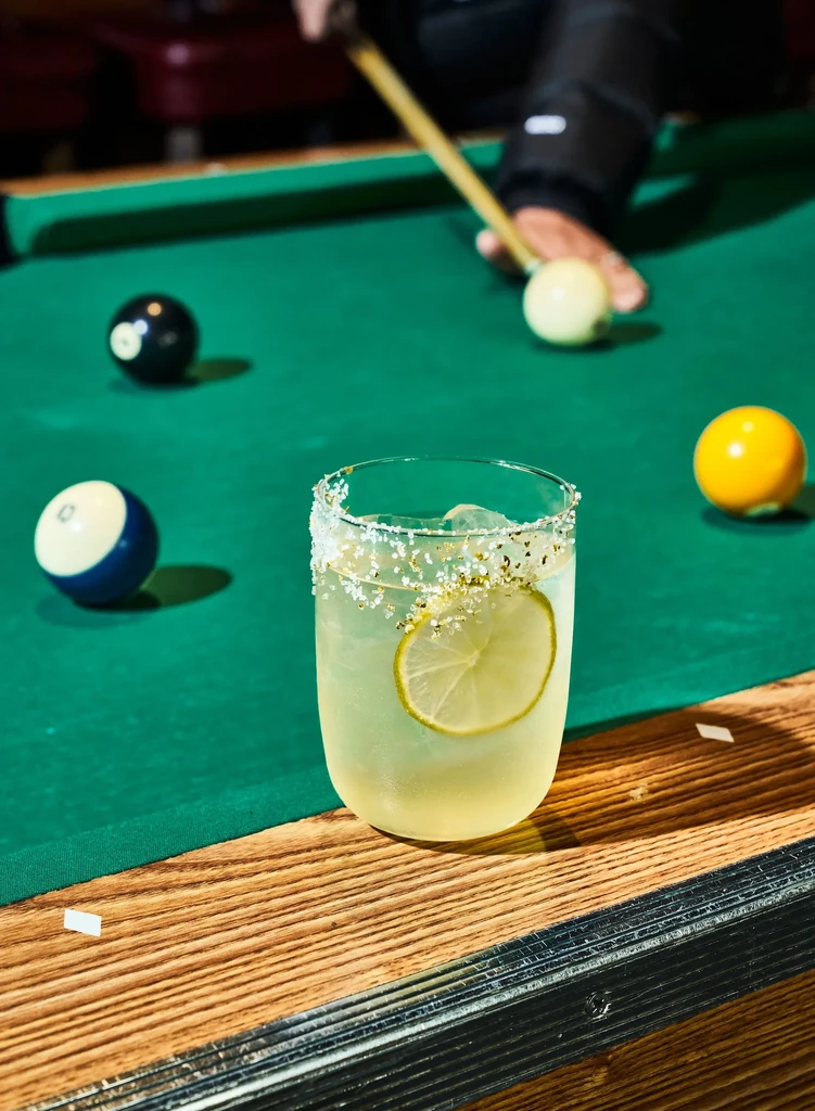 A margarita on a pool table with billiards being played.