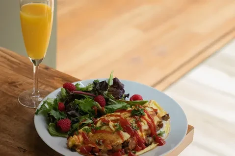 Omelet with ketchup, raspberries, and salad greens with orange juice.