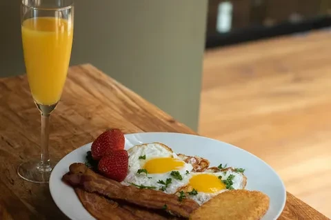 A breakfast plate with fried eggs, bacon, strawberries, and hash browns, plus orange juice.