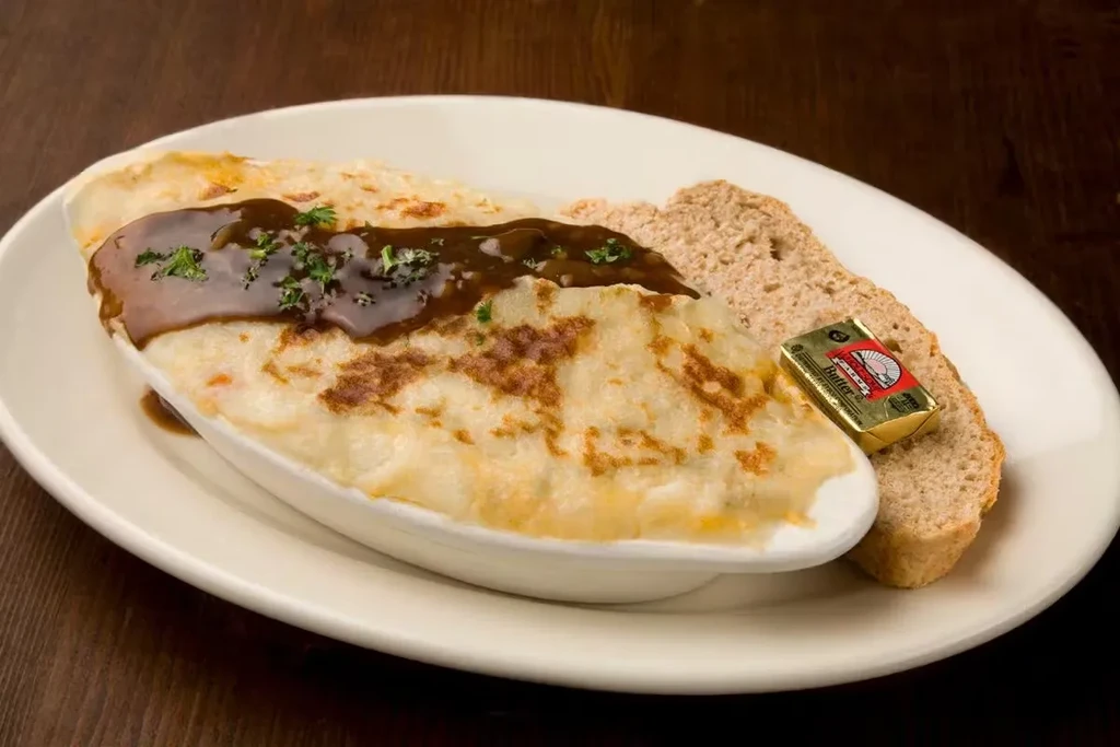Shepherd's pie with gravy and bread on a white plate.