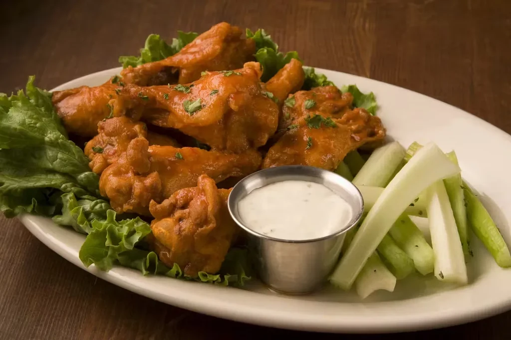 A plate of buffalo wings with ranch, celery, and lettuce.