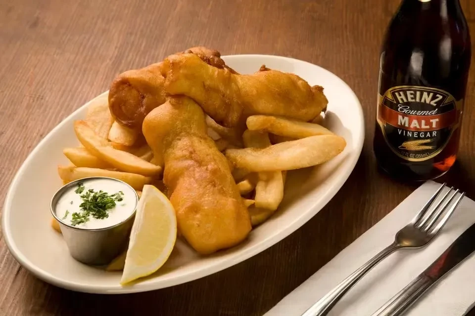 Fish and chips meal with tartar sauce, lemon, and malt vinegar.