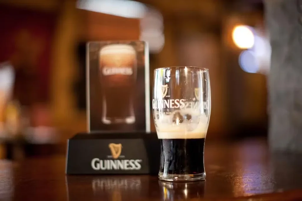 A half-full Guinness glass next to a Guinness advertisement on a bar.