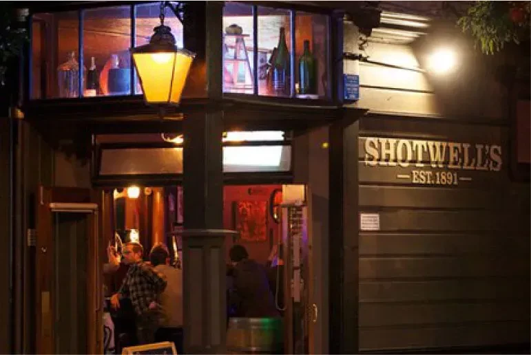Exterior of Shotwell's bar at night with customers inside.