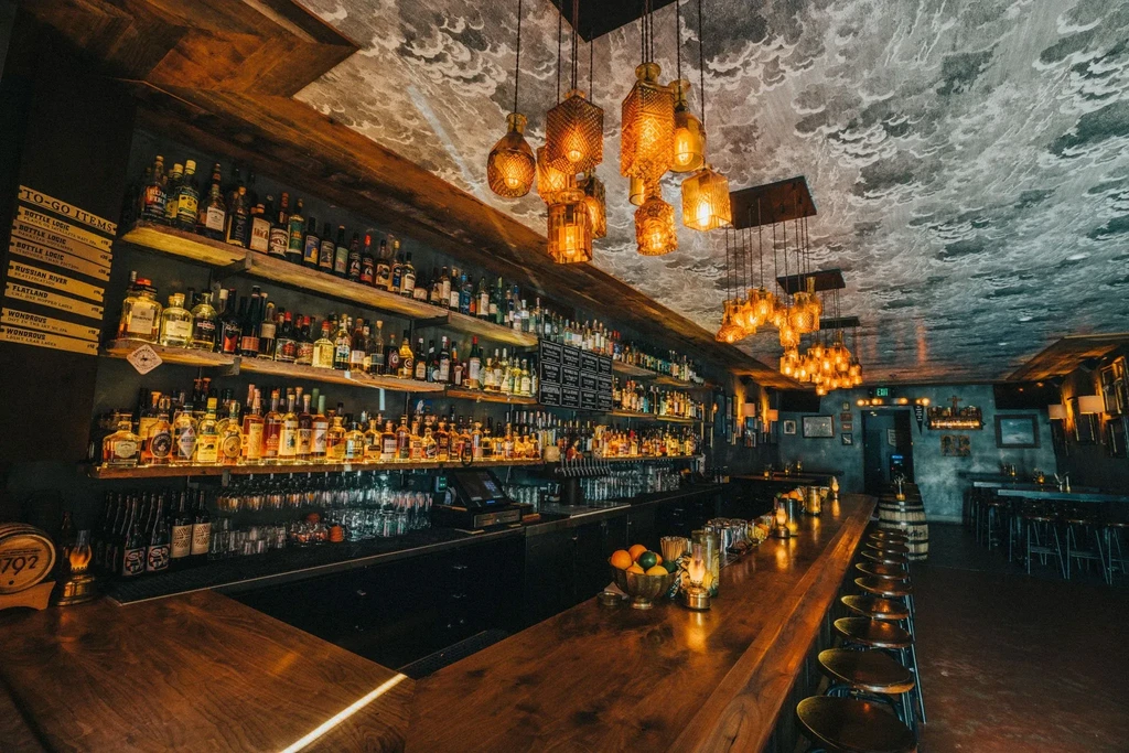 A well-stocked bar with a long wooden counter and many hanging lights.