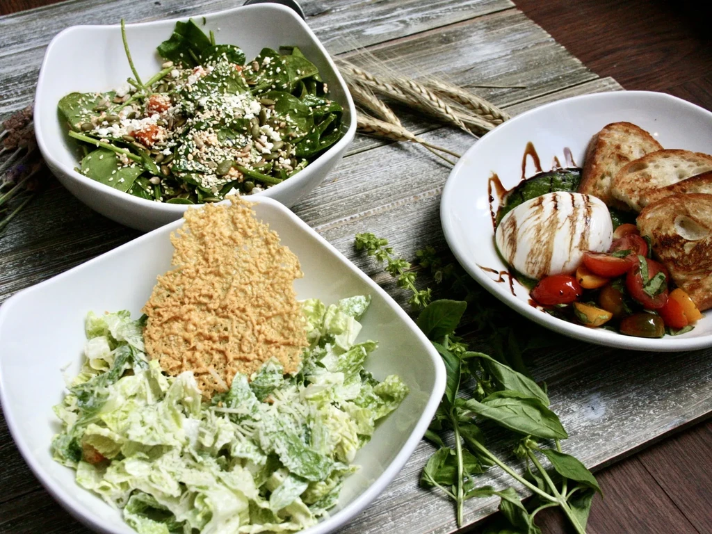 Three bowls of salad with burrata cheese, toast, and basil leaves.