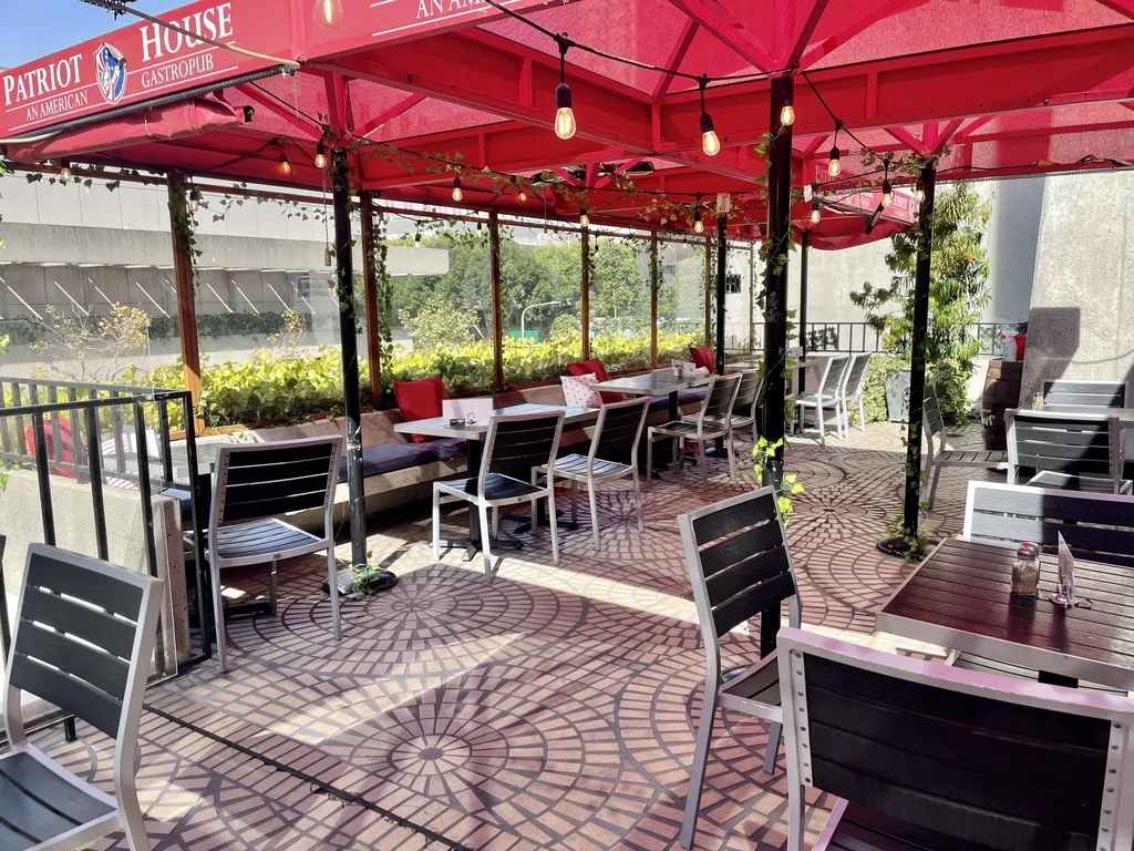 An outdoor patio with red umbrellas, tables, and chairs, with lush greenery.