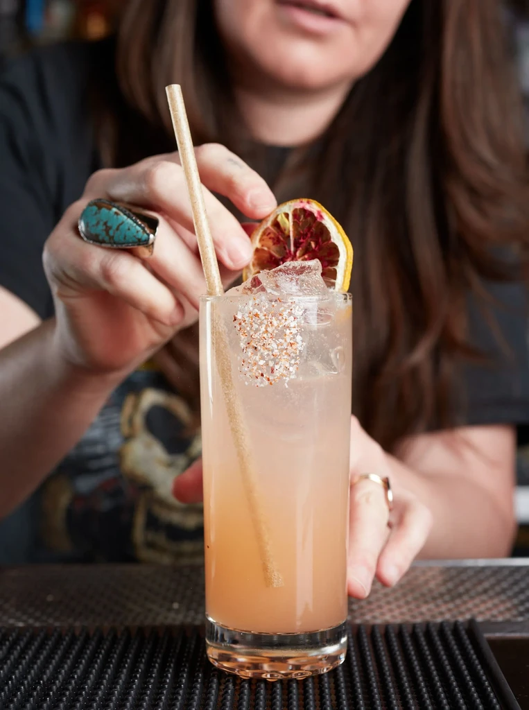 A bartender garnishes a tall pink cocktail with a dried orange slice.