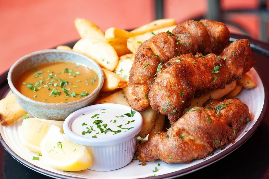 Golden-brown fried fish with fries, lemon wedges, and two sauces.