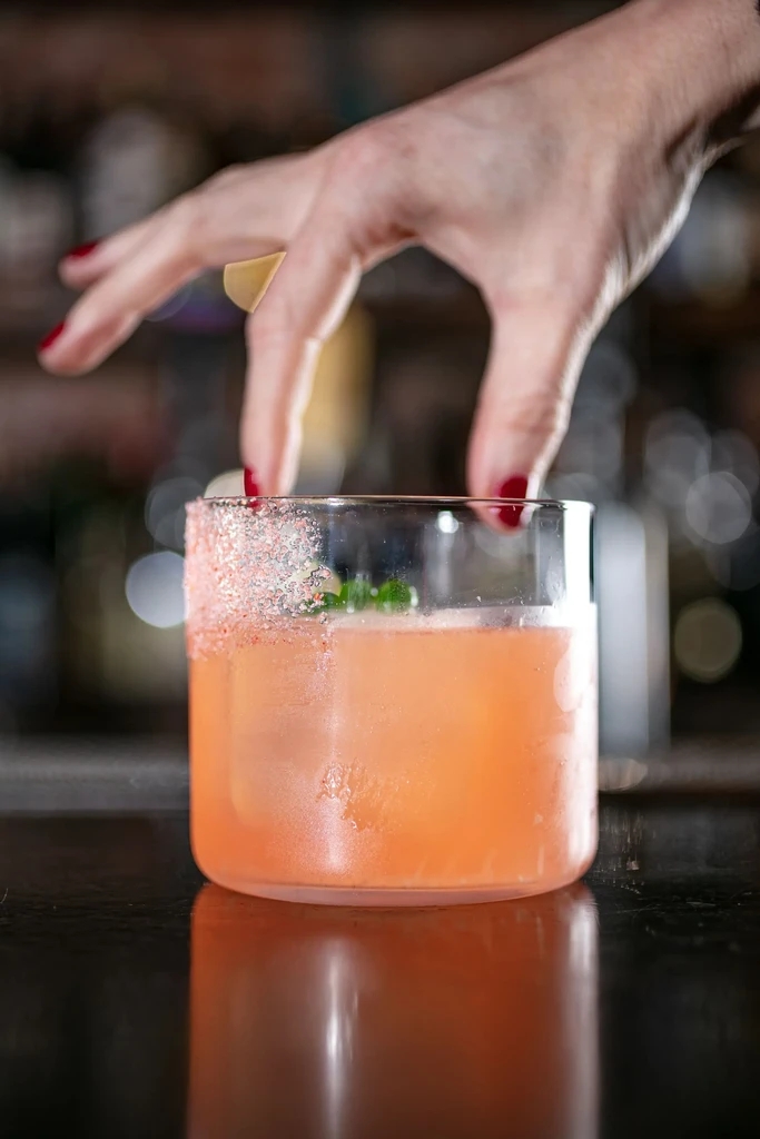Hand garnishing an iced pink cocktail with a salt rim.