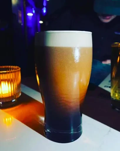 A pint glass of dark beer with a creamy head.