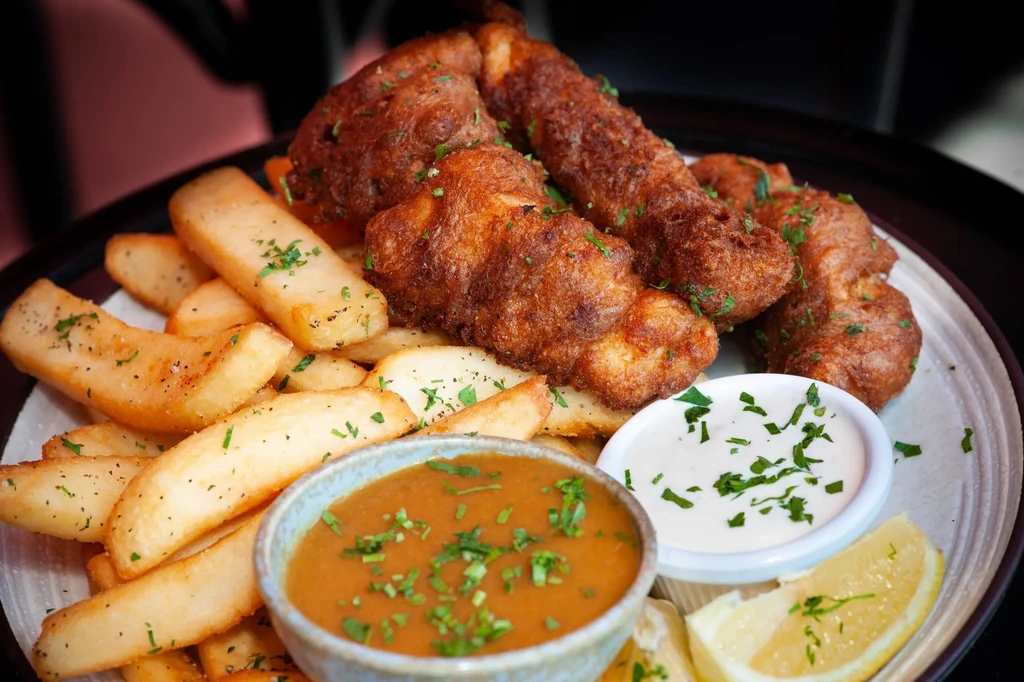 Fish and chips with gravy and tartar sauce on a white plate.
