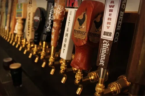 A row of beer taps on a dark bar with a small dark beer.