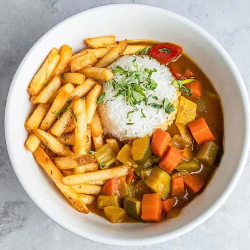 Fries, rice, and curry with vegetables in a white bowl.