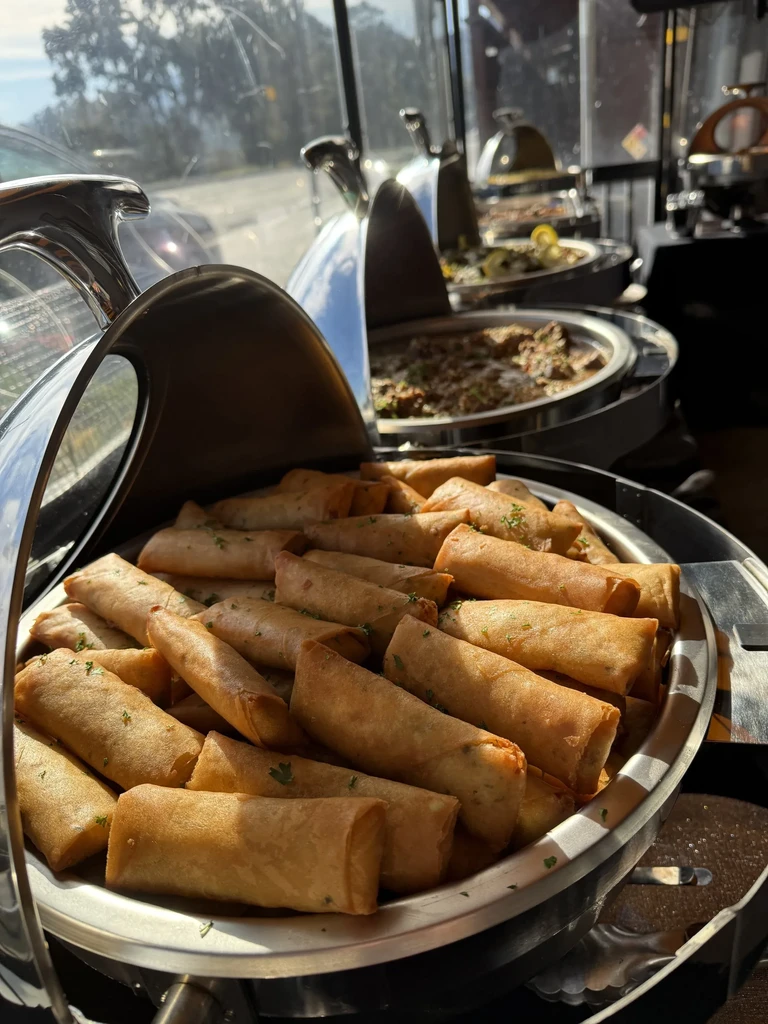 A chafing dish filled with golden-brown spring rolls, garnished with herbs.
