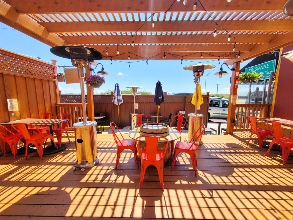 An outdoor restaurant patio with a wooden pergola and red chairs.