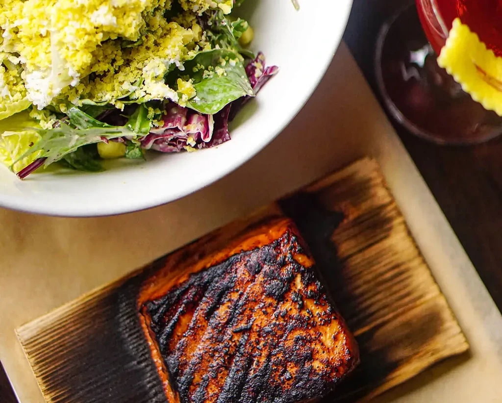 Grilled salmon on a cedar plank with a side salad and drink.