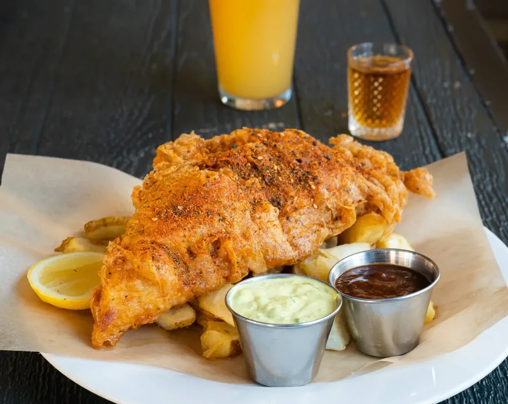 Crispy fried fish and chips with lemon, tartar sauce, and BBQ sauce.