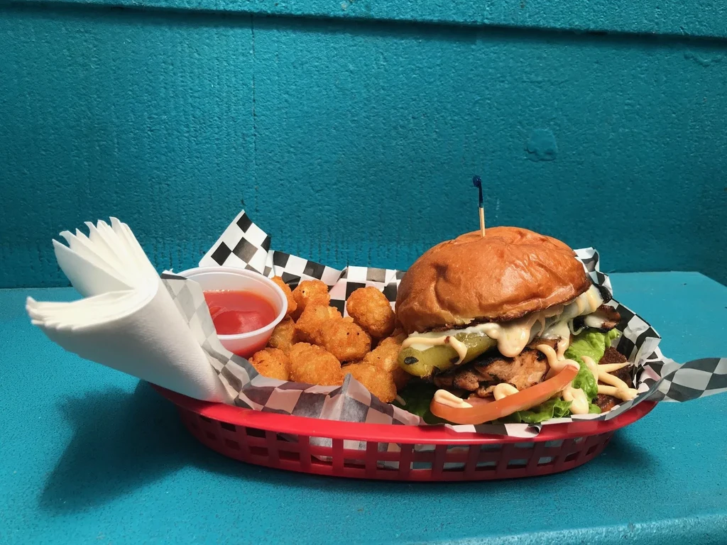A red basket with a burger, tater tots, ketchup, and napkins.