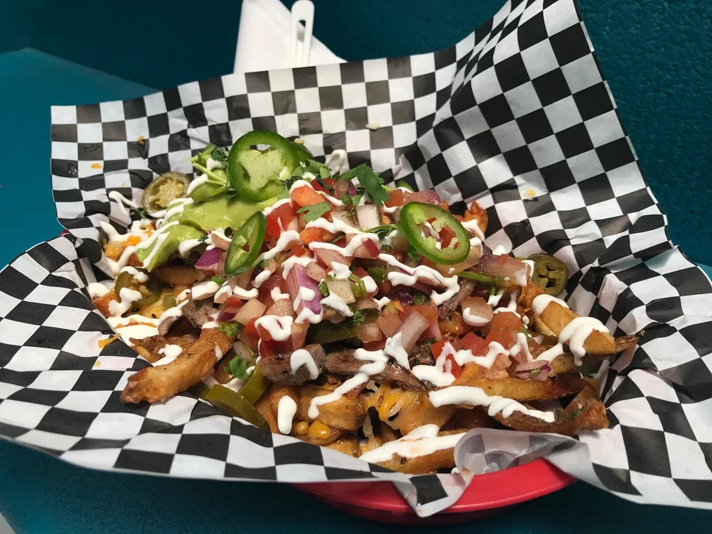 Loaded carne asada fries with pico de gallo and guacamole in a basket.