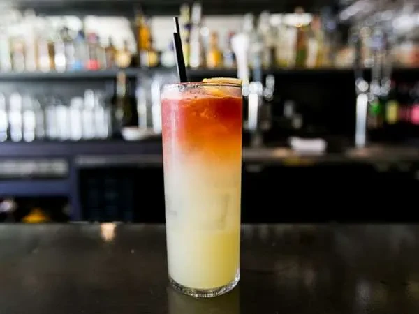 A tall glass with an orange and yellow layered cocktail.