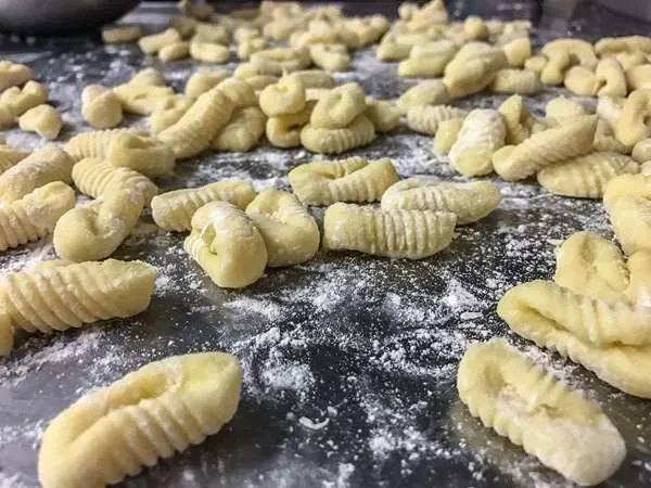Freshly made gnocchi, dusted with flour on a dark surface.