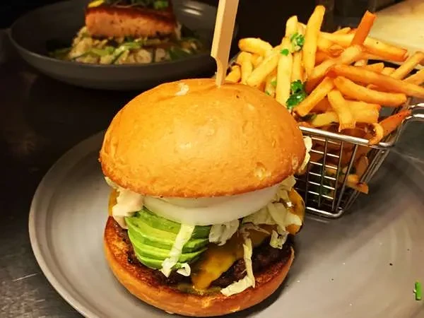 A burger with avocado, onion, lettuce, and fries on a gray plate.