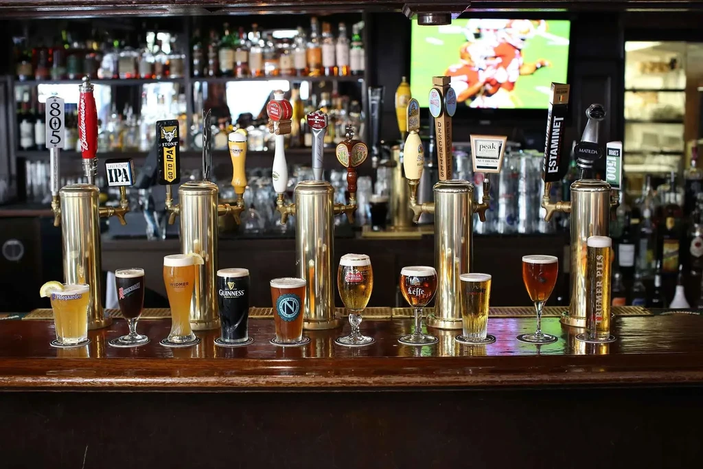 Nine different beers poured at a bar with taps in the background.