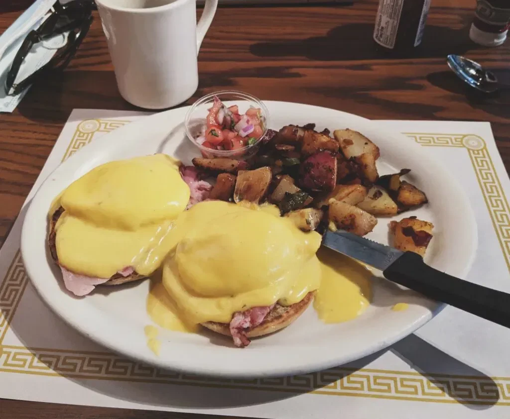 Eggs Benedict with home fries, salsa, and coffee on a table.