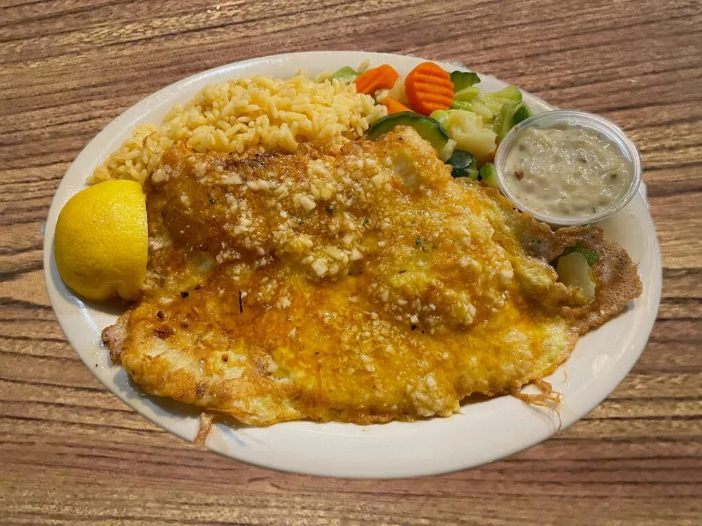A breaded fish fillet with rice, vegetables, and tartar sauce.