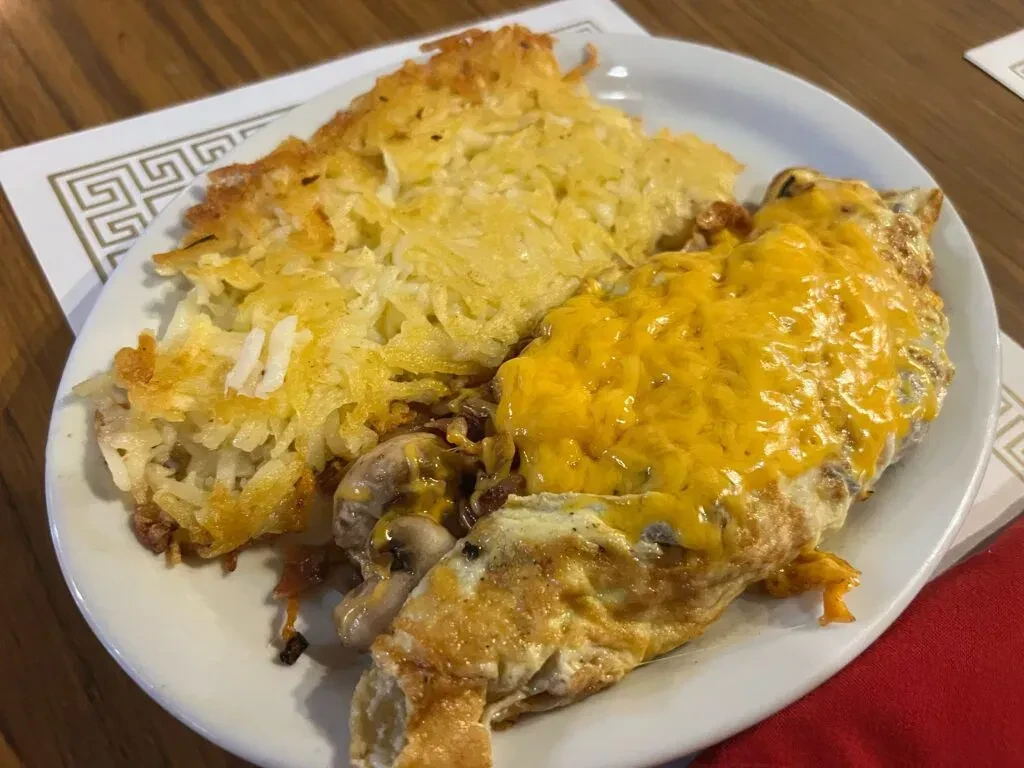 A plate of hash browns and a cheese omelet with mushrooms.