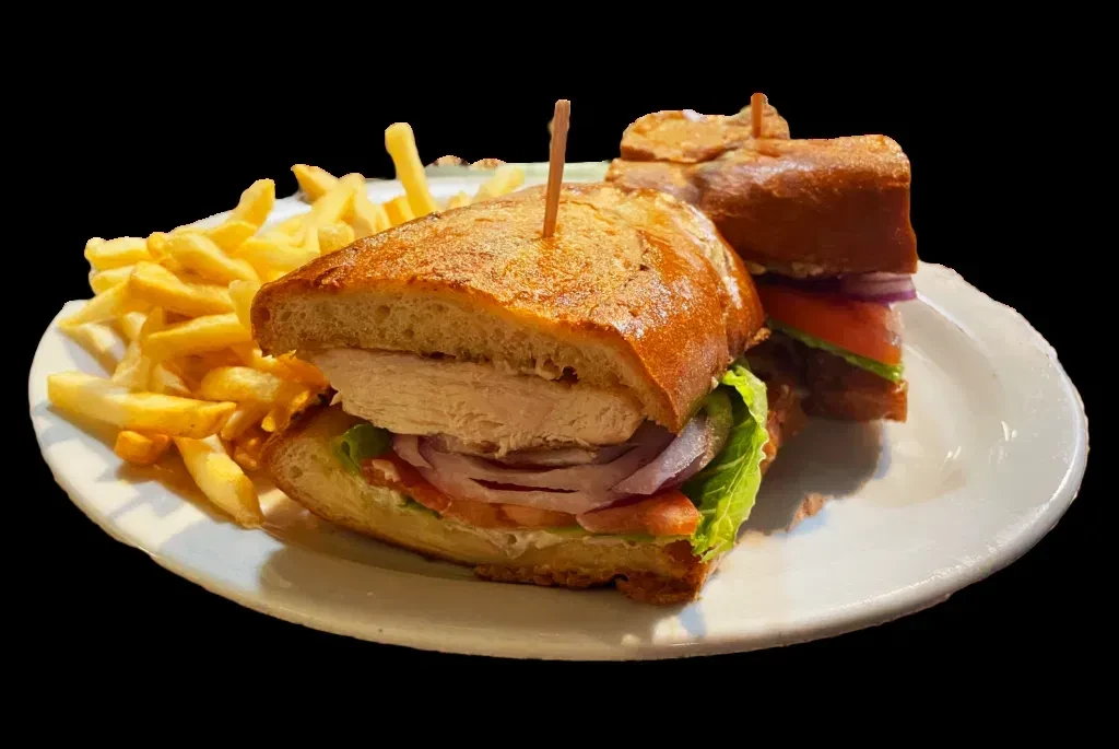 Chicken sandwich with lettuce, tomato, onions, and fries on a white plate.