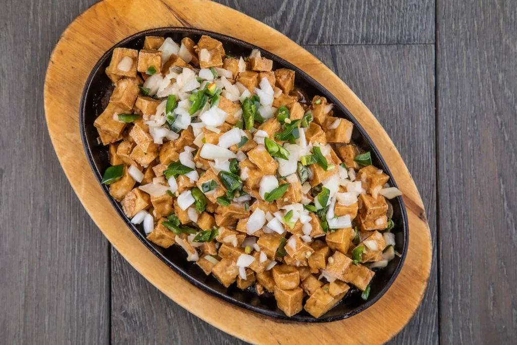 Fried tofu cubes with onions and jalapeños in a black skillet.