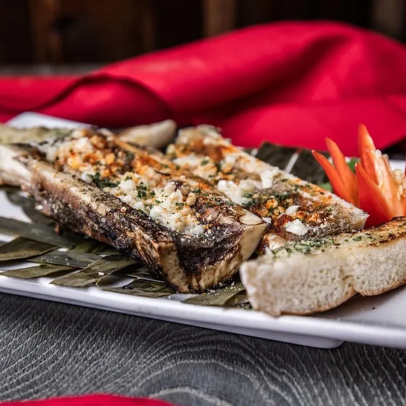 A plate of roasted bone marrow, topped with herbs and crushed nuts.