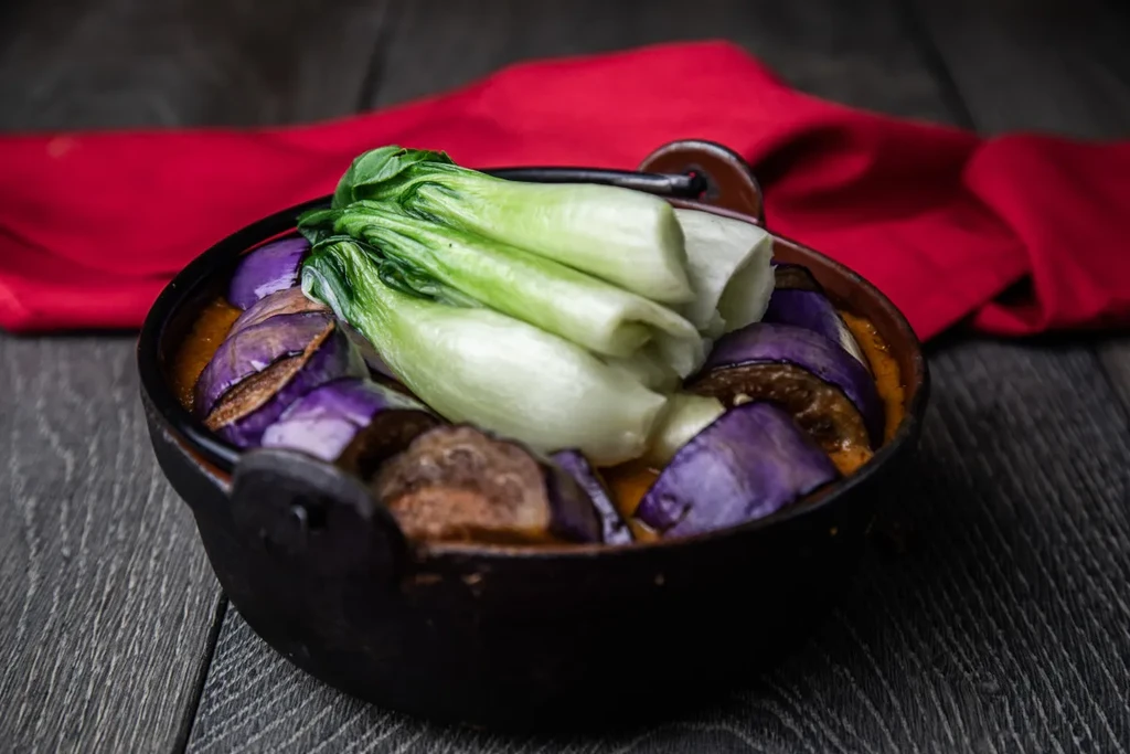 Stew with eggplant, bok choy, and meatballs in a black bowl.