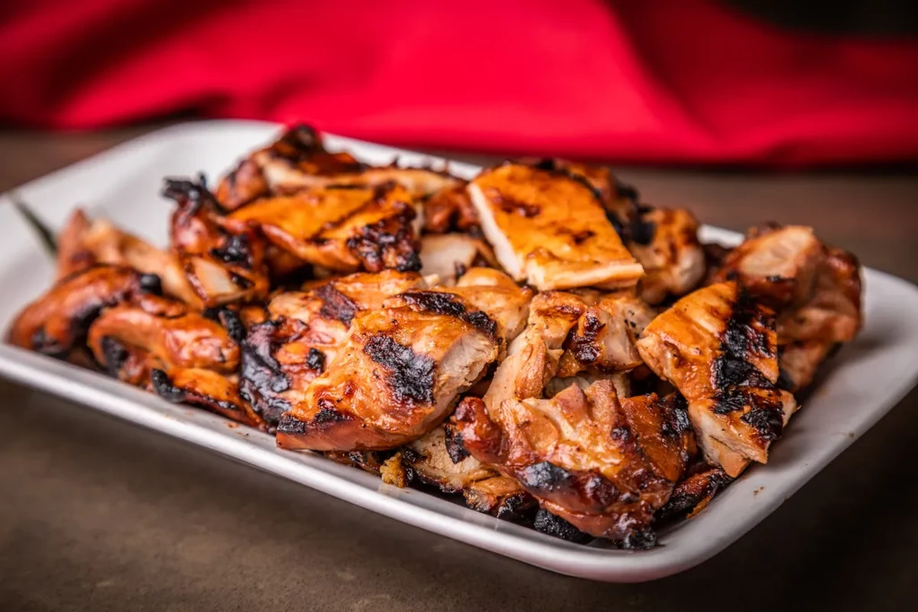 A white plate filled with charred, chopped grilled chicken pieces.