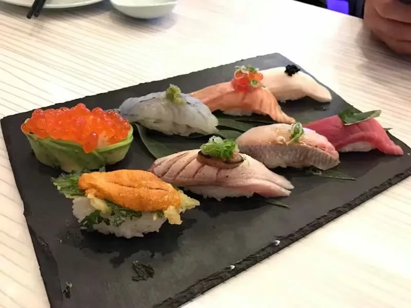 A black slate platter with seven pieces of varied nigiri sushi.