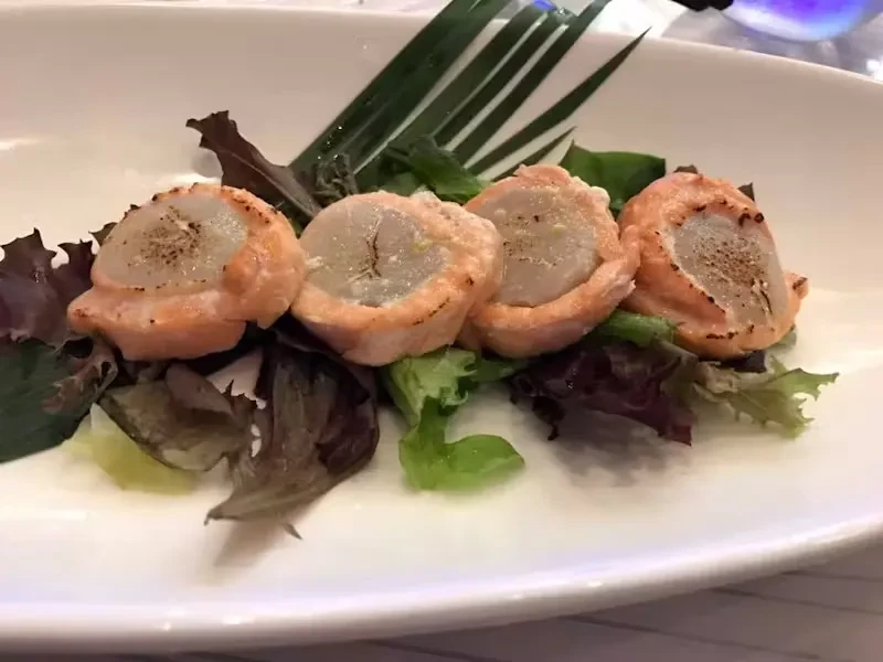 Four scallops wrapped in salmon on a bed of lettuce.