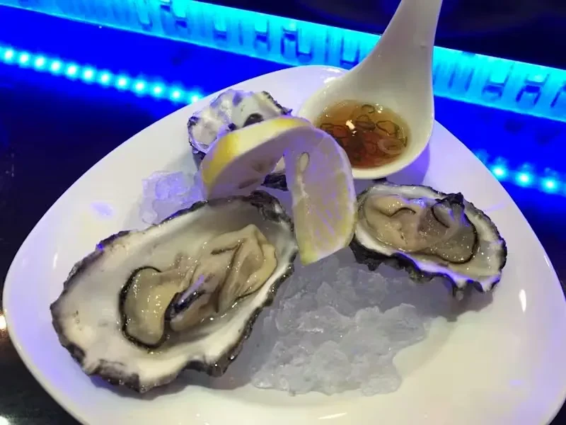 Three oysters on ice with lemon and sauce on a white plate.