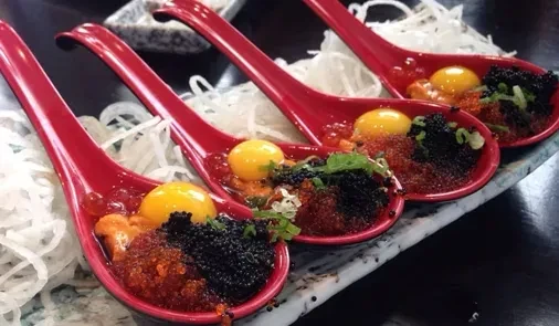 Four red spoons holding caviar, quail egg yolks, and garnishes.
