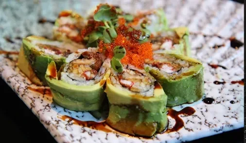 Green sushi rolls with orange roe and microgreens on a marble plate.
