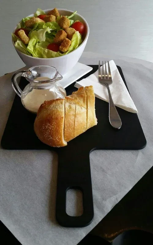 Salad with dressing and sliced bread on a black serving board.