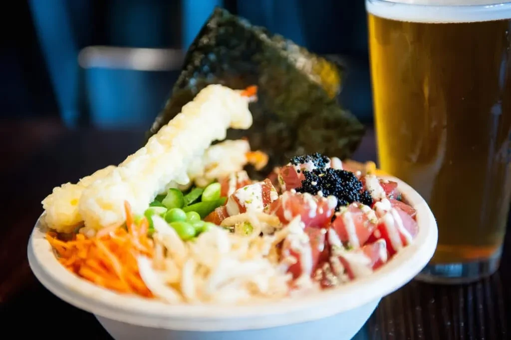 A poke bowl with tuna, tempura, vegetables, black roe, and a beer.