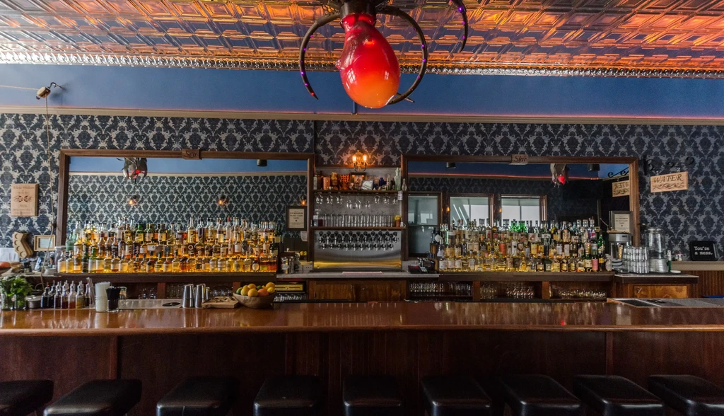 A bar interior with bottles of alcohol and a red overhead light.