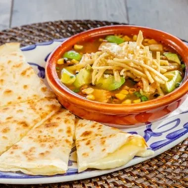 Quesadillas next to a bowl of soup topped with tortilla strips and avocado.